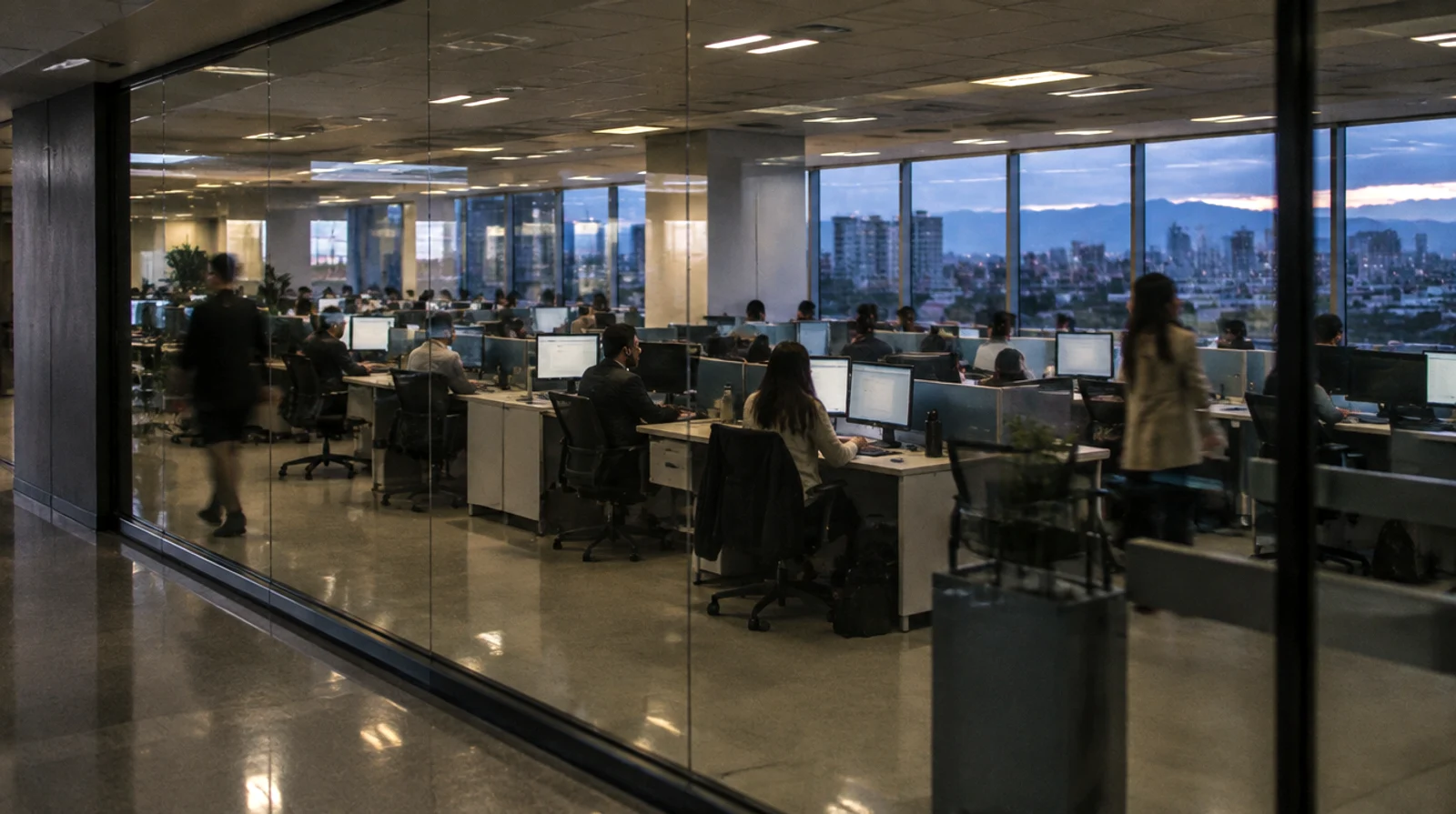 Piso de operaciones de atención de un banco al anochecer, visto a través de una mampara de vidrio